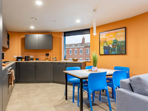 A kitchen with orange walls and a dining table with blue chairs.