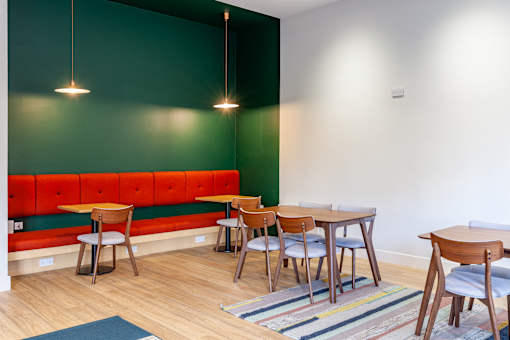 A room with a green wall and a bench with chairs and tables.