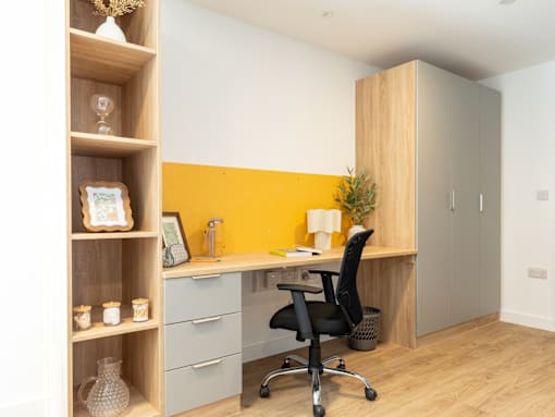 A yellow accent wall behind a desk with a black chair.