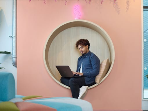 A man is sitting on a circular chair with a laptop.