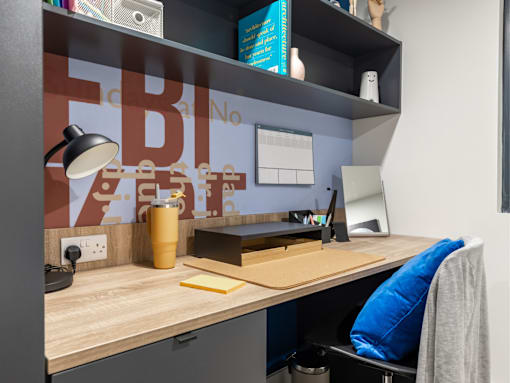 A desk with a lamp, a cup, and a notepad on it.