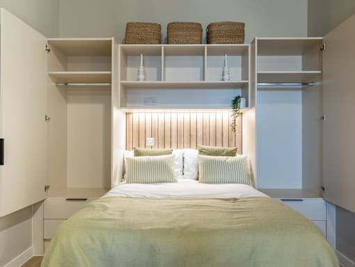 A bedroom with a bed, pillows, and shelves above it.