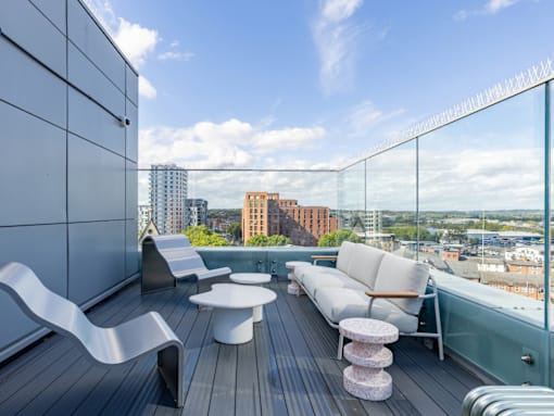 A white sofa with a wooden armrest sits on a wooden deck with a glass railing.