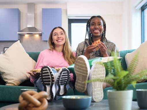 Two people are sitting on a couch with their feet up, eating pizza and enjoying a relaxed moment together.