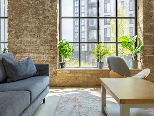A living room with a grey couch, a wooden table, and a large window.