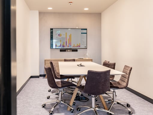 A conference room with a table, chairs, and a screen displaying graphs.