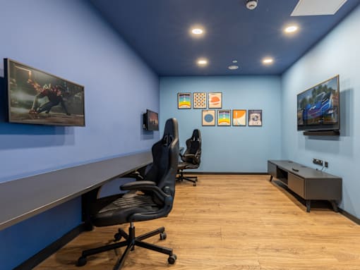 A room with blue walls and wooden floors has a desk, chairs, and pictures on the wall.