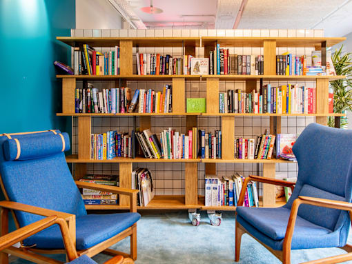 Two blue chairs are in front of a bookshelf filled with books.