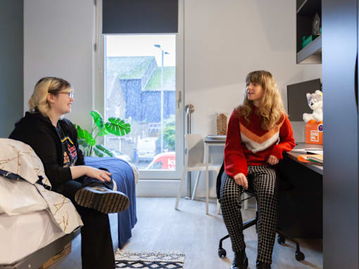 Two women sitting in a room with a window in the background.