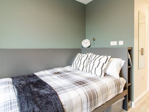 A bed with a plaid comforter and striped pillows in a room with green walls.