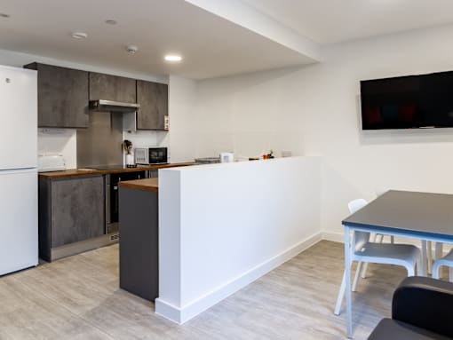 A modern kitchen with a white refrigerator, a microwave, and a dining table with chairs.