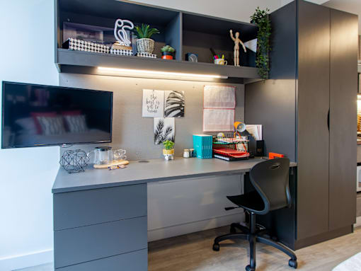 A modern home office with a grey desk, black chair, and shelves with various items.