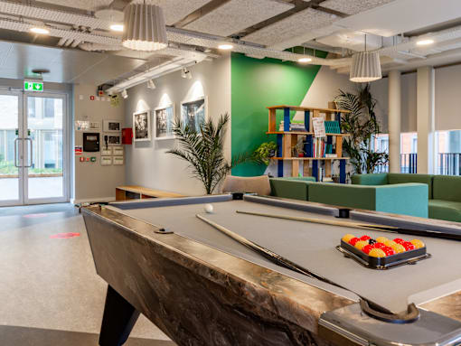 A pool table is in the middle of a room with a green wall and a bookshelf.
