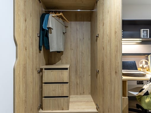 A wooden closet with clothes hanging and drawers underneath.