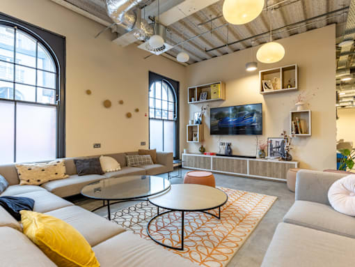A living room with a grey couch, a white sofa, a round table and a TV mounted on the wall.