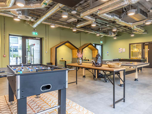 A foosball table is in the middle of a room with a ping pong table and a long table with chairs.