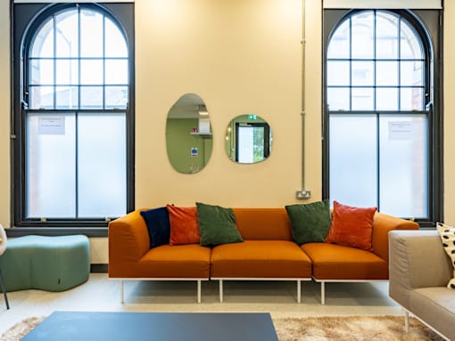 A living room with a large orange couch and two round mirrors on the wall.