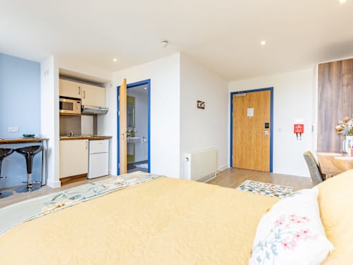 A bedroom with a bed in the foreground and a kitchen area in the background.