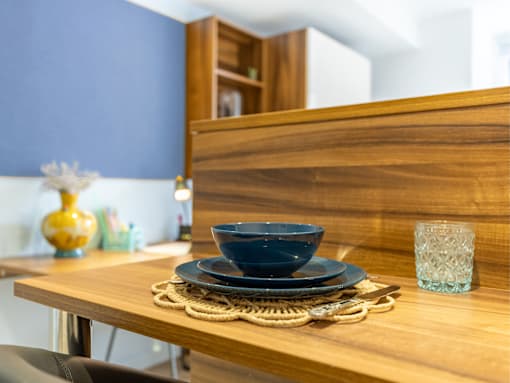 A wooden table with a blue bowl, a glass, and a yellow vase on it.