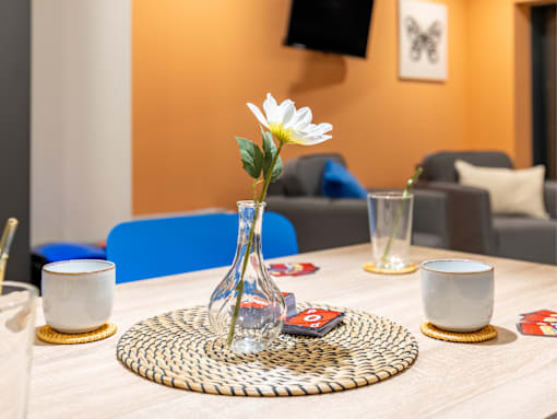 A table with a vase of flowers, two cups, and a coaster with a card on it.