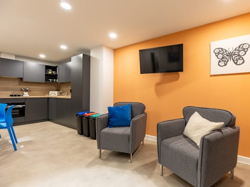 Two grey armchairs with blue pillows are placed in a room with orange walls.