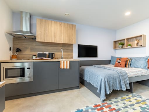 A modern kitchen with a microwave, oven, and a bed in the same room.