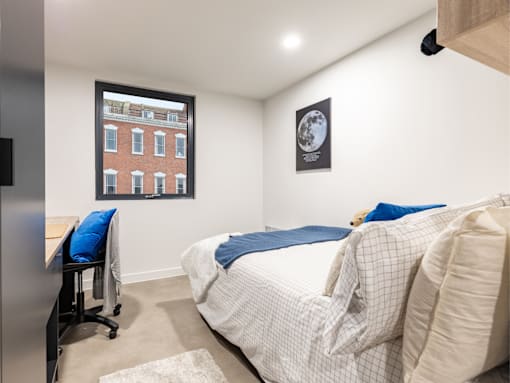 A bedroom with a bed, desk, and window.