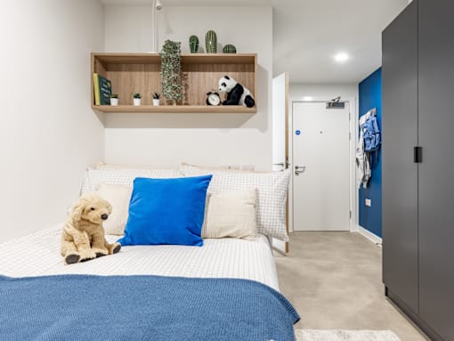 A bedroom with a bed, a teddy bear, and a shelf with plants and a stuffed panda bear.