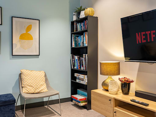 A living room with a chair, a bookshelf, a lamp, and a TV displaying the NETFLIX logo.
