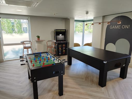 A foosball table is in the middle of a room with a ping pong table and a TV.