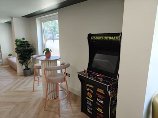 A Legends Ultimate arcade machine sits in a room with a potted plant and two chairs.