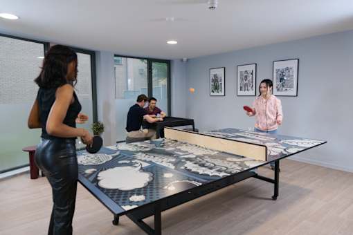 A woman in a black dress is playing a game on a large table with a man in a pink shirt and two other people in the background.
