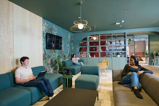A man is sitting on a blue couch using a laptop.