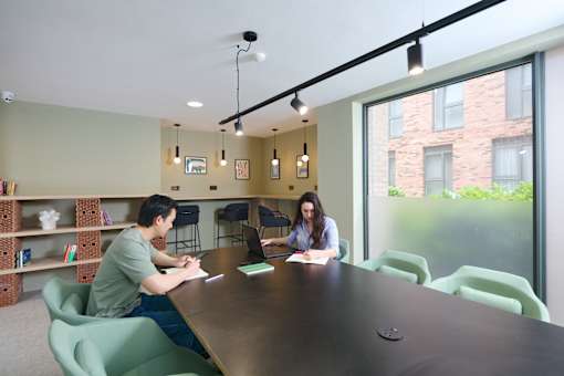 Two people sitting at a table in a room with a window overlooking a brick building.