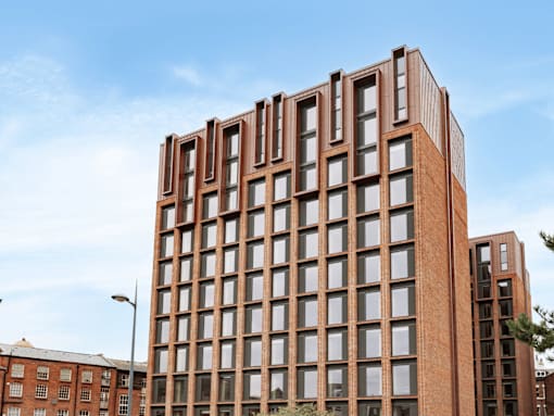 A tall red brick building with many windows stands in front of a blue sky.