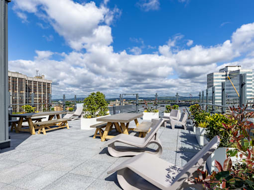 A rooftop patio with tables and chairs overlooking a cityscape.
