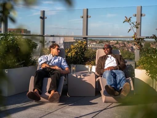 Two men are sitting on chairs on a rooftop terrace.