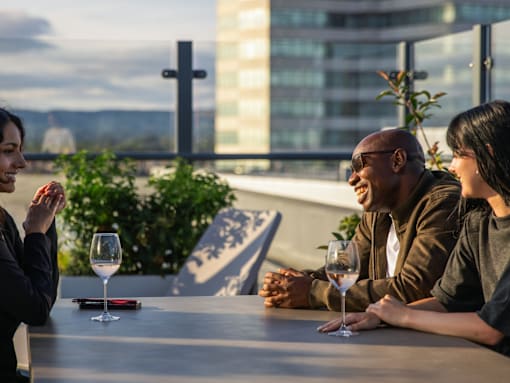 Three people sitting at a table with wine glasses in front of them.