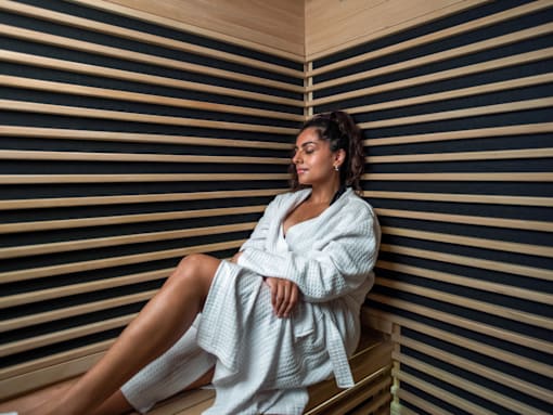 A woman in a white robe is sitting in a sauna.