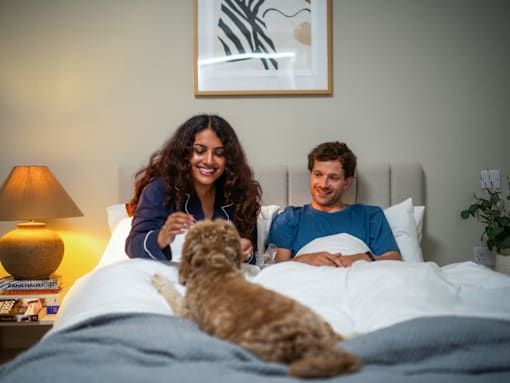 A man and woman are sitting on a bed with a dog.