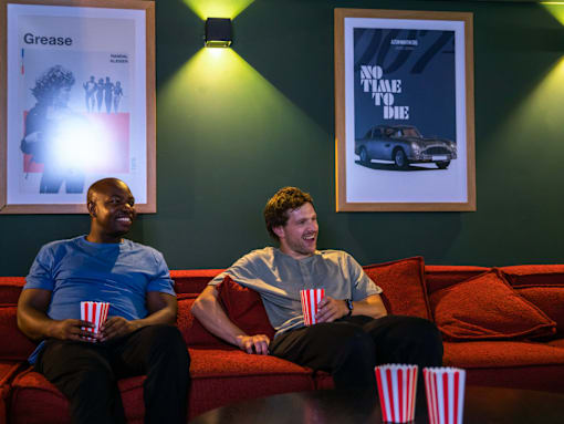 Two men sitting on a couch with popcorn and watching a movie.