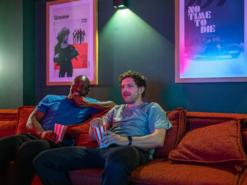 Two men are sitting on a couch with popcorn containers in front of them.