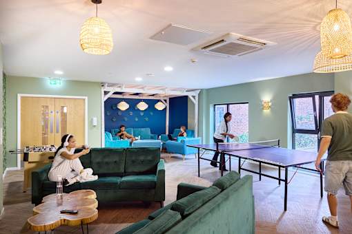 A man is playing ping pong in a room with a woman sitting on a couch.