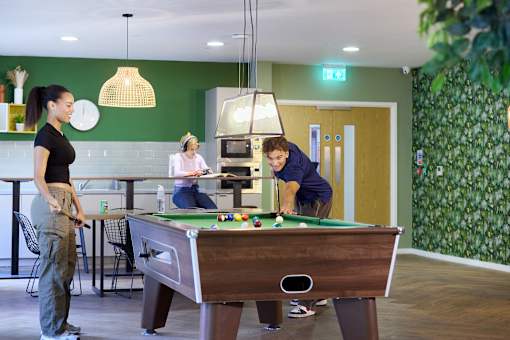 Three people playing pool in a room with a green wall.