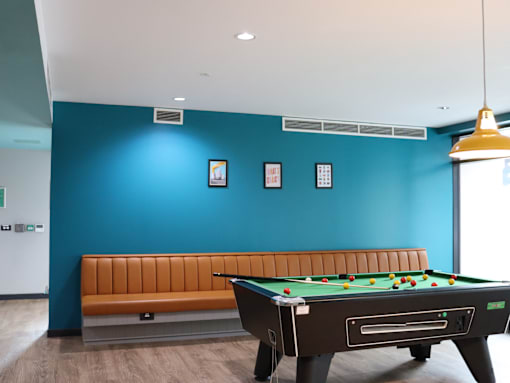 A pool table with a bench in front of a blue wall.