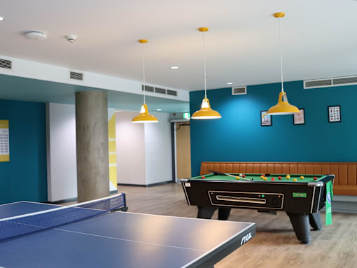 A pool table is in the middle of a room with a ping pong table in front of it.