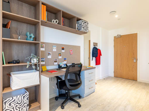 A room with a desk, chair, and shelves with various items.
