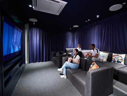 Two people are sitting on a couch in a room with purple curtains.