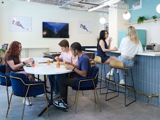 A group of people are sitting around a table in a room with a blue wall and a TV screen.