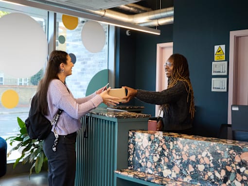 A woman in a pink shirt is handing over a document to another woman at a reception desk.